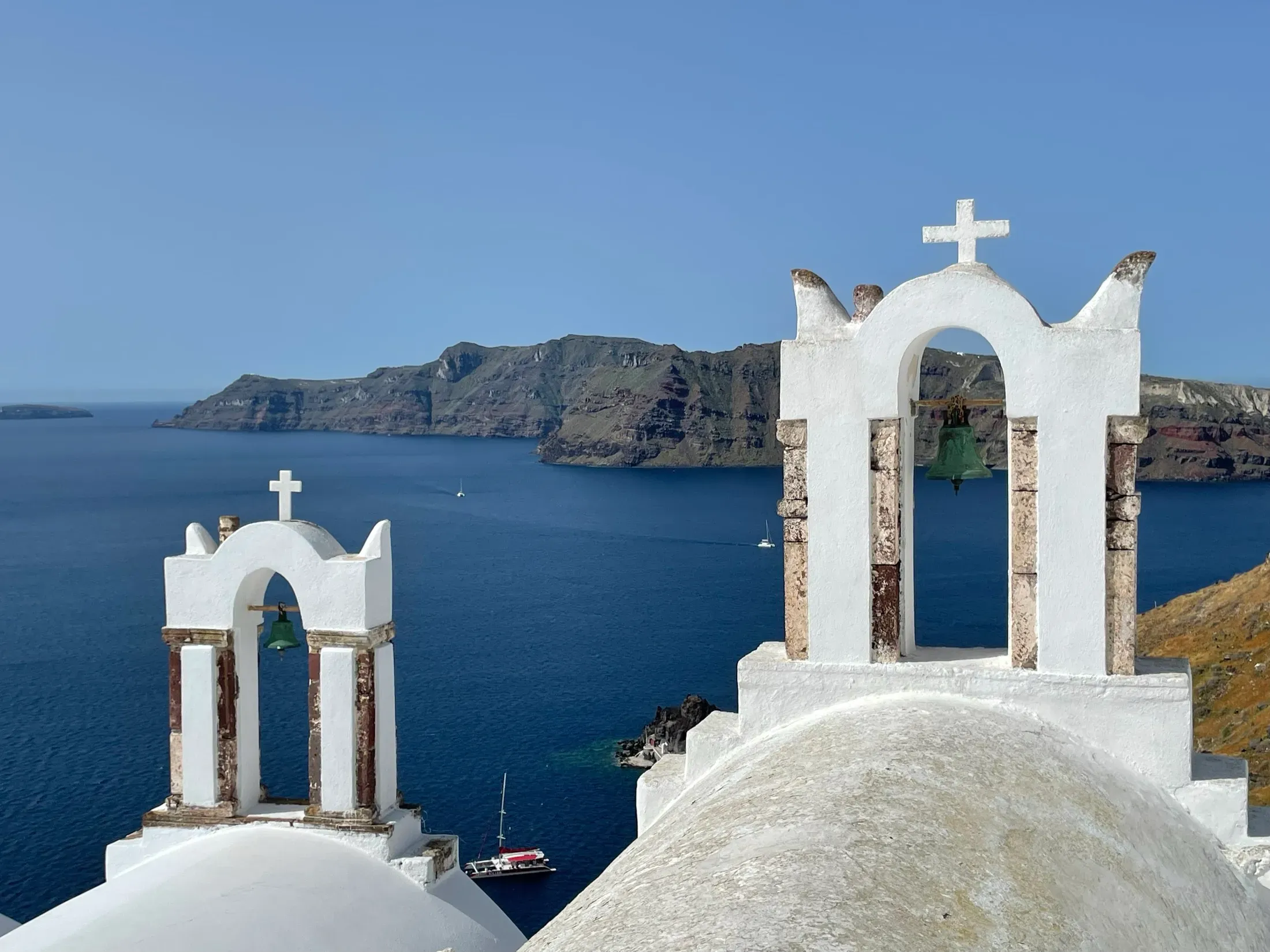 A whitewashed Greek church with bells and a blue dome above the Aegean